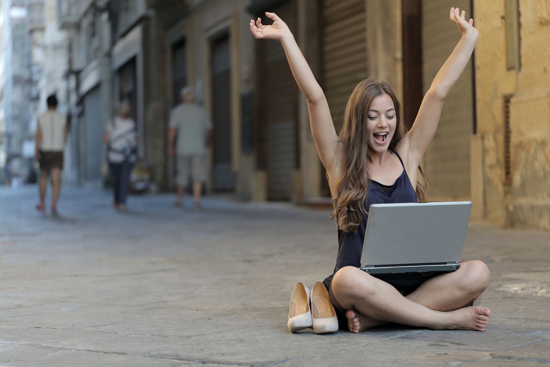 Frau mit Laptop sitzt auf dem Gehweg und jubelt