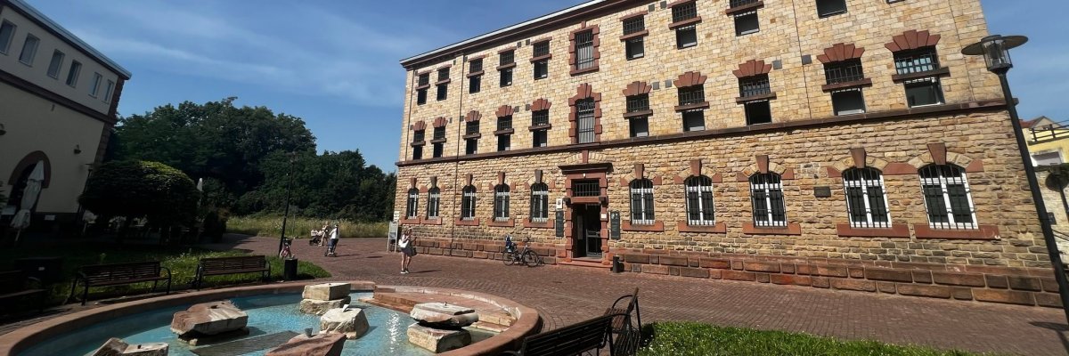 Frontansicht des ehemaligen Arrestgebäude mit dem Brunnen vorm Eingang