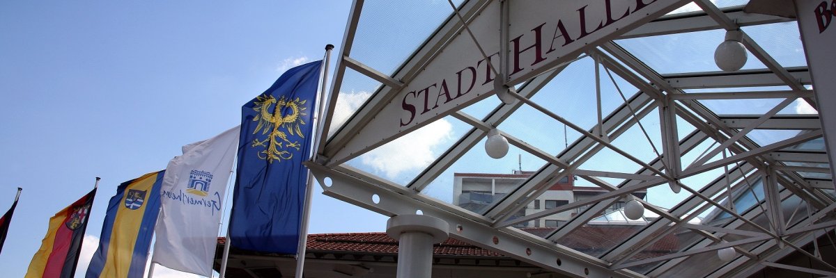 Glasüberdachung des Eingangs der Stadthalle mit verschiedenen Stadt-Flaggen im Hintergrund