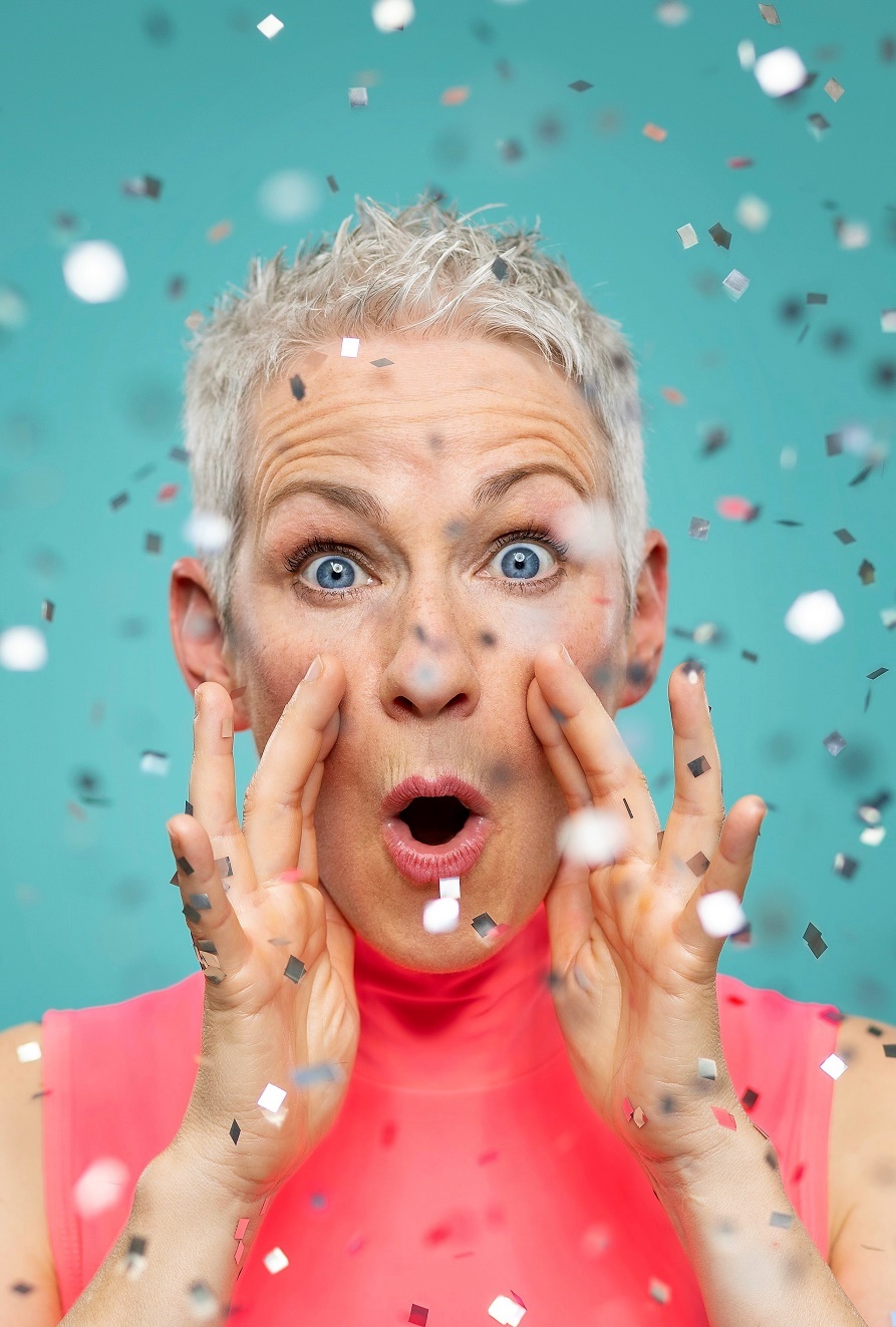 Tina Häussermann schaut direkt in die Kamera und ruft etwas. Um Sie herum fällt silbernes Glitzerpapier in kleinen Stückchen herab.
