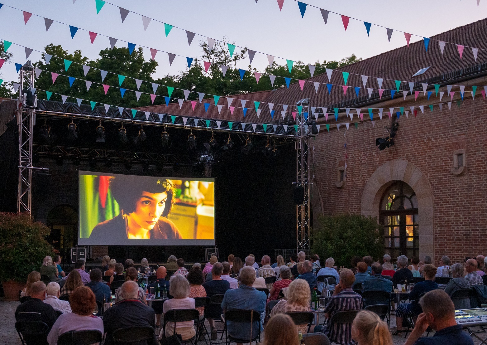 Foto aus dem Kulturzentrum Hufeisen; es ist die Filmleinwand zu sehen, davor sitzen die Besucher an Bistrotischen und schauen zur Leinwand