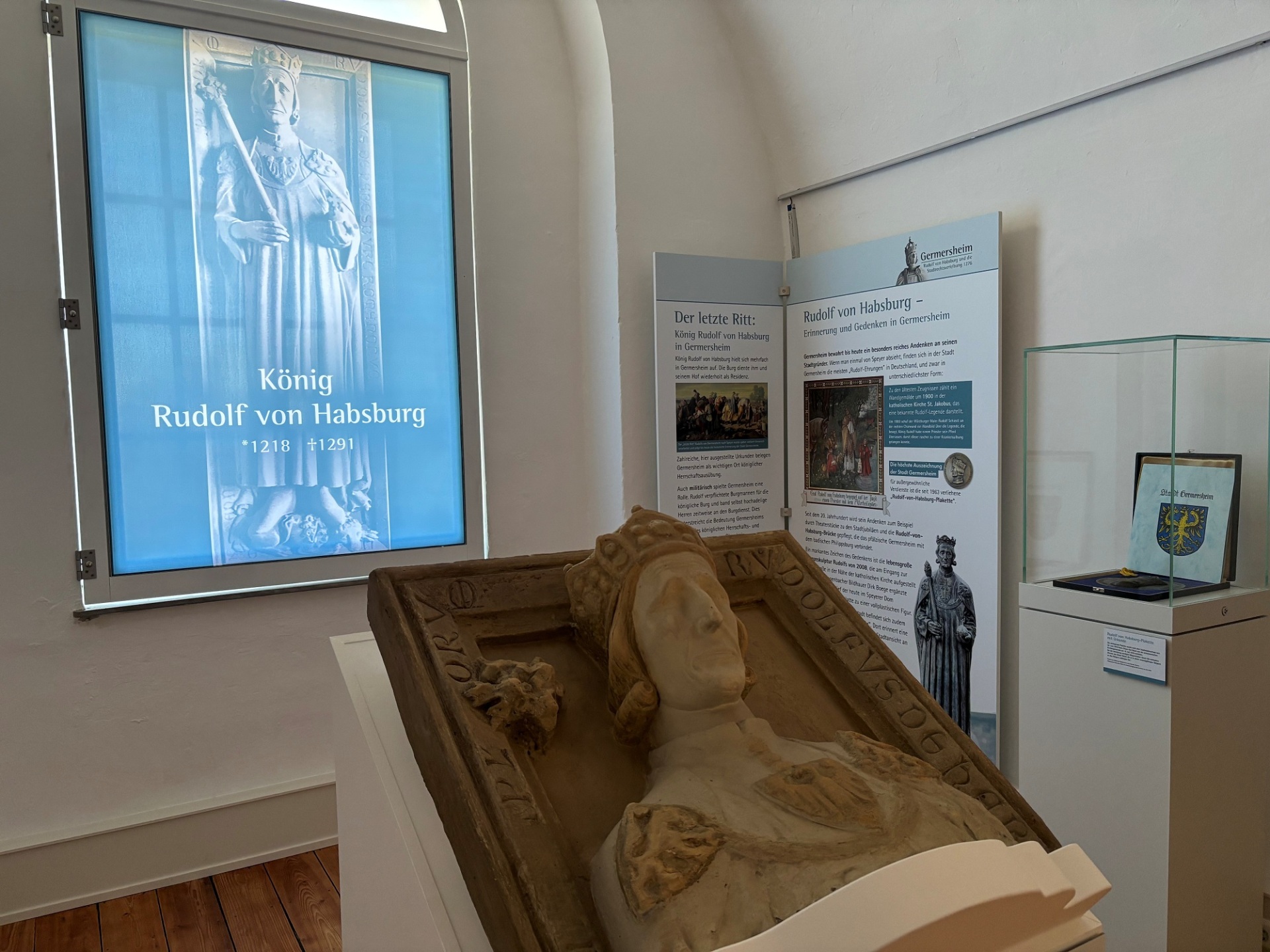 Foto aus der aktuellen Ausstellung; Steinbildnis von Rudolf von Habsburg vor einer Projektion mit dem Titel der Ausstellung