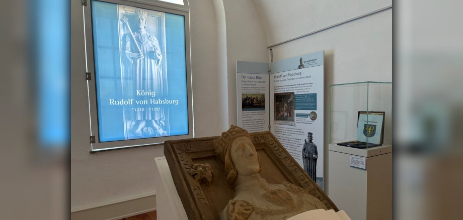 Foto aus der aktuellen Ausstellung; Steinbildnis von Rudolf von Habsburg vor einer Projektion mit dem Titel der Ausstellung