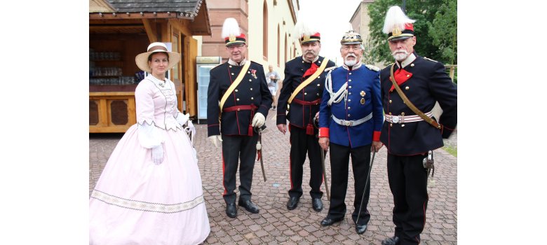 Eine Frau in historischem Kleid mit Hut, vier Männer in verschiedenen historischen Militäruniformen