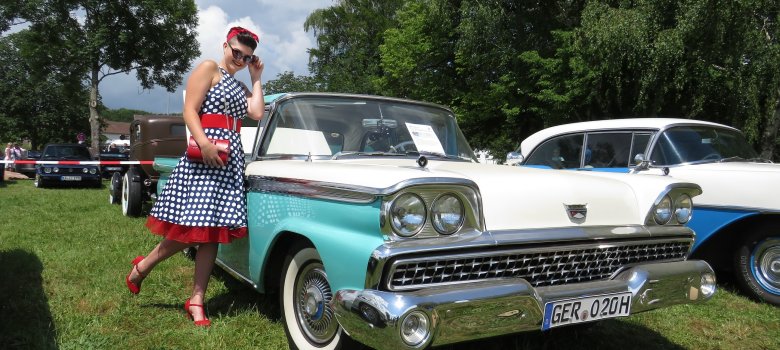 Frau in Pünktchenkleid neben eine Oldtimer Auto mit Lack in türkis/creme