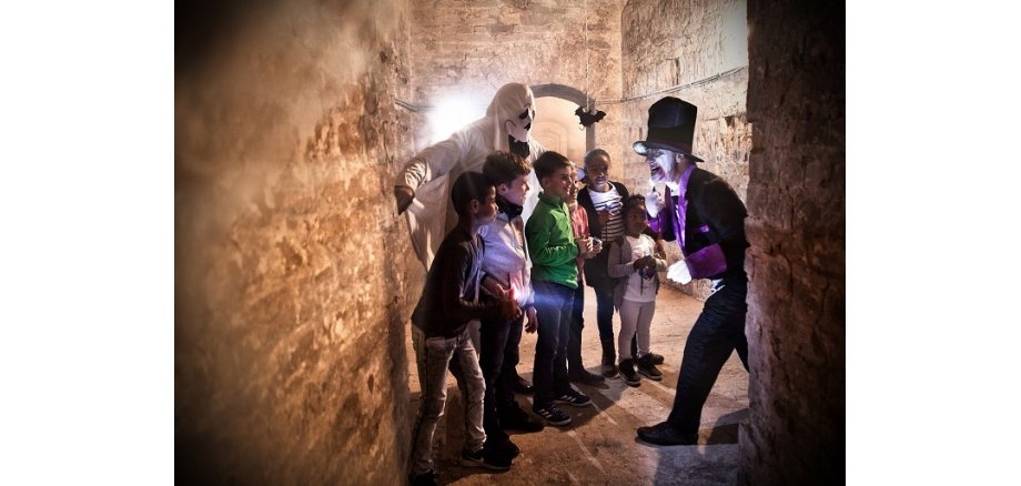 Gruppe von Kindern mit Gespenst und Zauberer bei einer Gruselführung in den Festungsgängen